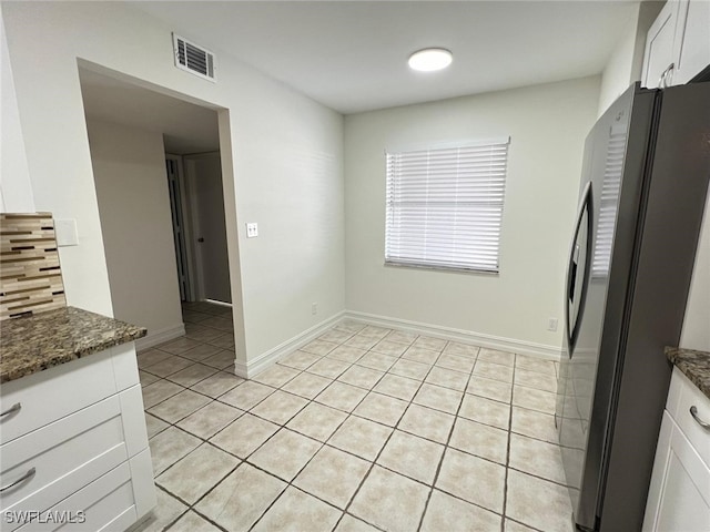 kitchen with decorative backsplash, stainless steel refrigerator, white cabinets, light tile patterned floors, and dark stone countertops