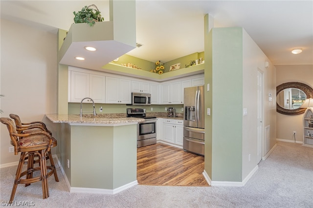 kitchen featuring kitchen peninsula, white cabinetry, light carpet, a breakfast bar, and appliances with stainless steel finishes