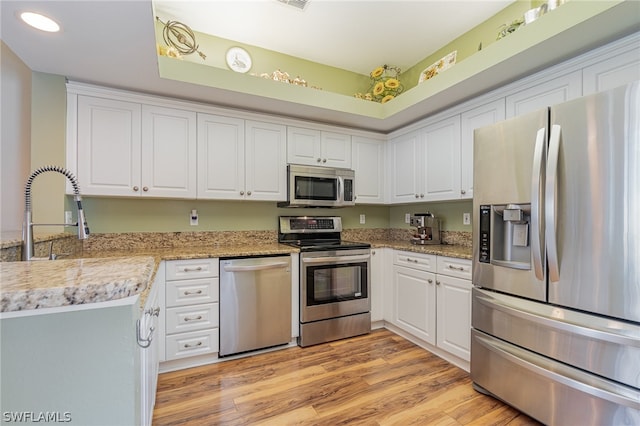 kitchen with white cabinets, light hardwood / wood-style flooring, light stone counters, and stainless steel appliances