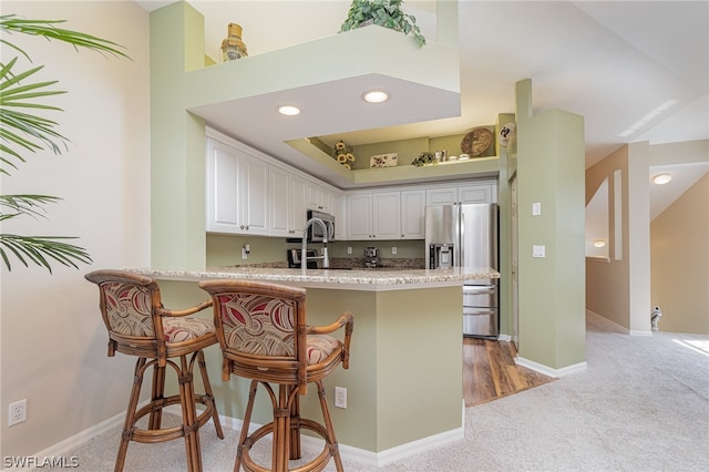 kitchen with a kitchen breakfast bar, white cabinets, carpet floors, and stainless steel appliances