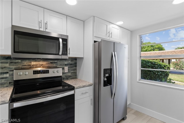 kitchen with a healthy amount of sunlight, appliances with stainless steel finishes, light stone counters, and white cabinets