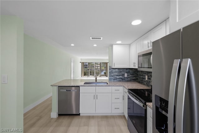 kitchen featuring tasteful backsplash, white cabinetry, light wood-type flooring, appliances with stainless steel finishes, and sink