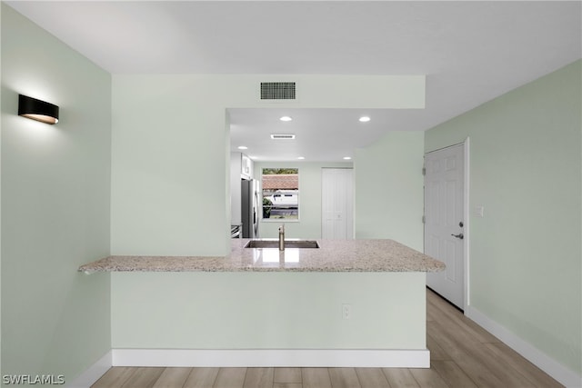 kitchen with sink, kitchen peninsula, light stone countertops, and light hardwood / wood-style flooring