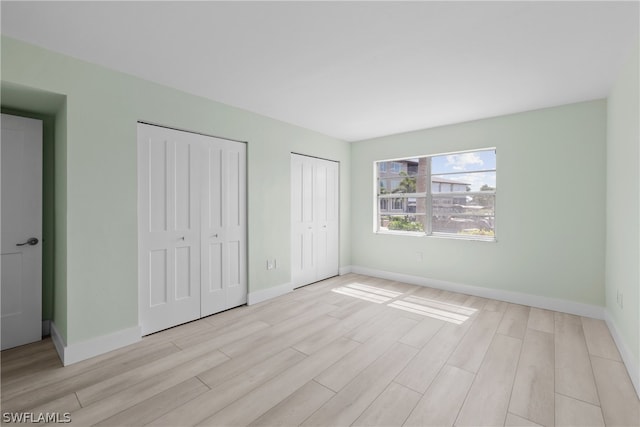 unfurnished bedroom with light hardwood / wood-style floors and multiple closets