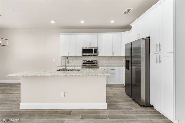 kitchen with light stone counters, appliances with stainless steel finishes, white cabinets, sink, and backsplash