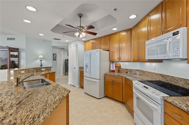 kitchen with sink, white appliances, ceiling fan, light stone counters, and a tray ceiling