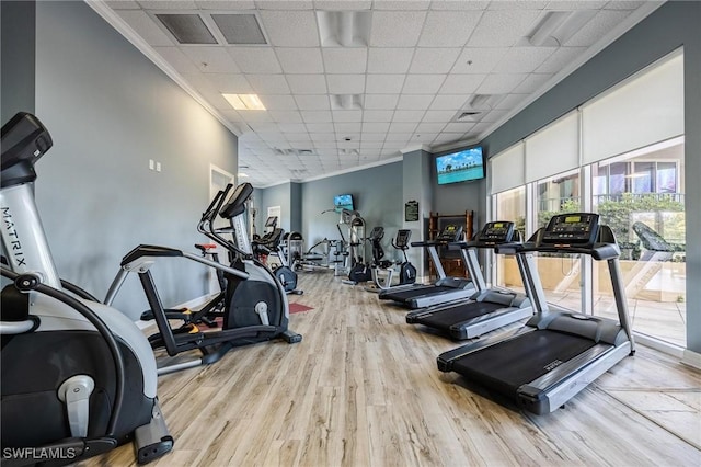 workout area featuring a paneled ceiling, ornamental molding, and light wood-type flooring