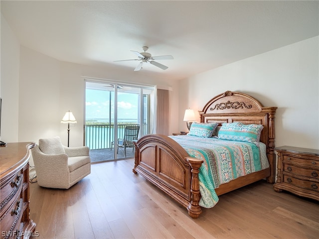 bedroom with access to outside, light hardwood / wood-style flooring, ceiling fan, and a water view