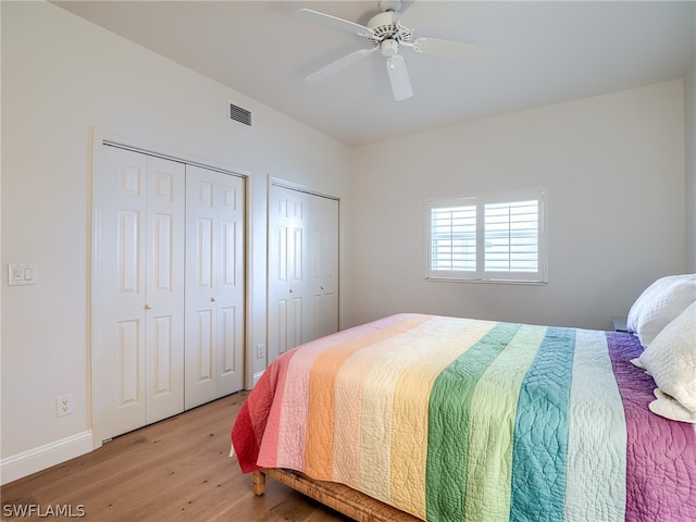 bedroom featuring light hardwood / wood-style flooring, ceiling fan, and multiple closets