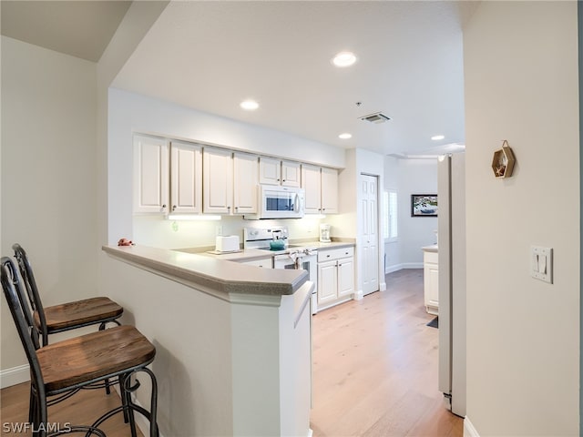 kitchen featuring kitchen peninsula, white appliances, light hardwood / wood-style floors, and white cabinetry