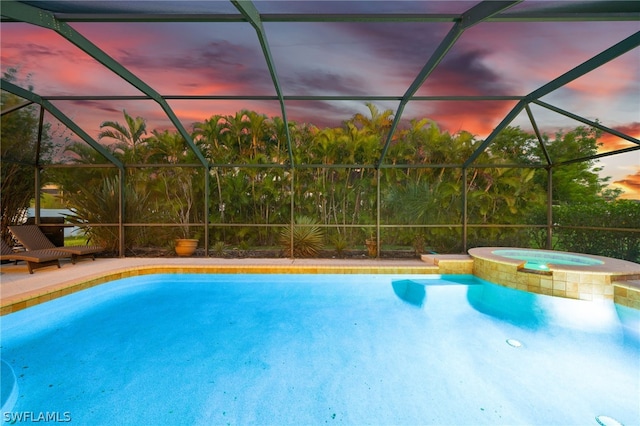 pool at dusk with an in ground hot tub and a lanai