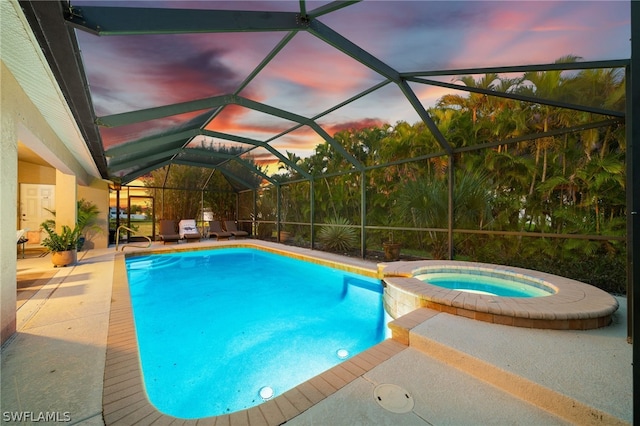 pool at dusk with an in ground hot tub, a patio, and glass enclosure