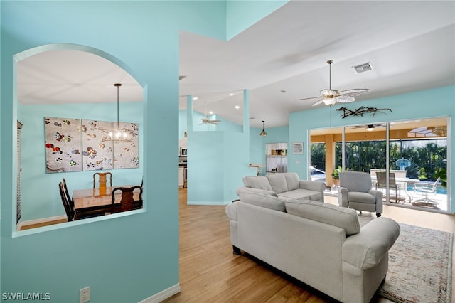 living room featuring ceiling fan with notable chandelier, light hardwood / wood-style flooring, and vaulted ceiling