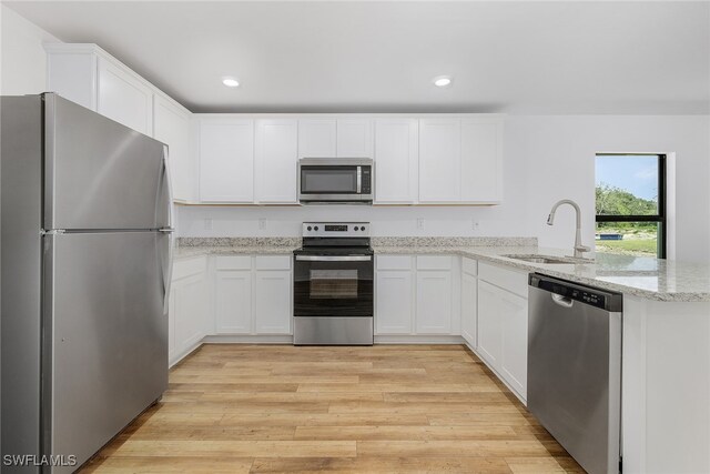 kitchen featuring light wood-type flooring, stainless steel appliances, light stone counters, kitchen peninsula, and sink