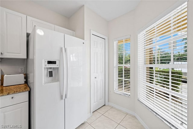 kitchen featuring light tile floors, white cabinetry, dark stone countertops, and white fridge with ice dispenser