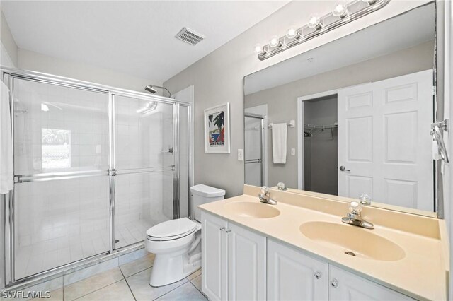 bathroom featuring double vanity, toilet, tile floors, and a shower with door