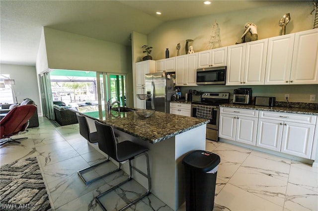 kitchen with white cabinets, a kitchen island with sink, a breakfast bar, and appliances with stainless steel finishes