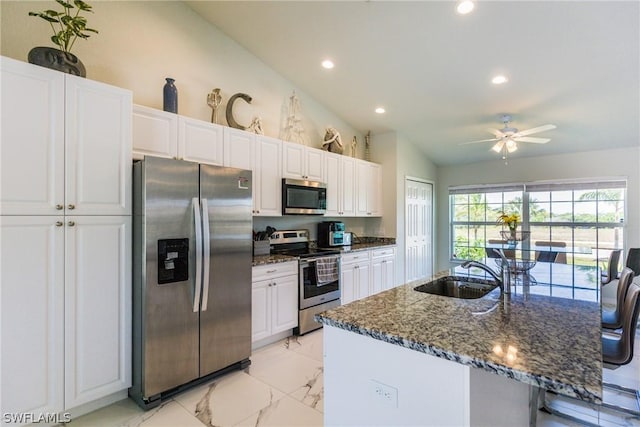 kitchen with appliances with stainless steel finishes, white cabinetry, sink, vaulted ceiling, and a center island with sink