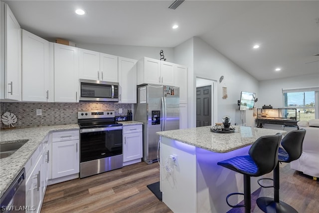 kitchen with white cabinets, appliances with stainless steel finishes, vaulted ceiling, hardwood / wood-style flooring, and tasteful backsplash