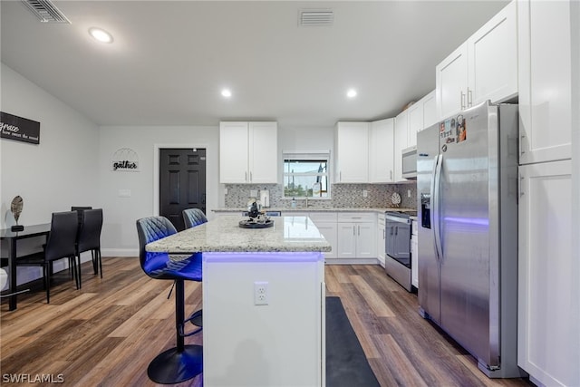 kitchen with stainless steel appliances, dark hardwood / wood-style floors, white cabinetry, a kitchen breakfast bar, and a center island