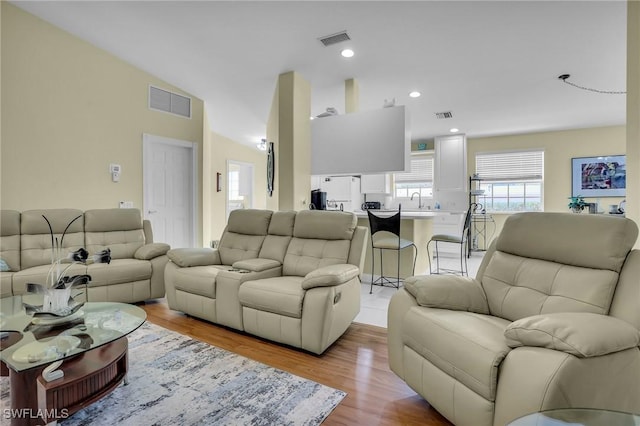 living room with lofted ceiling, sink, and light hardwood / wood-style flooring