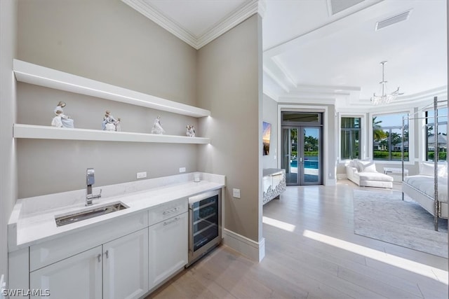 interior space with a chandelier, beverage cooler, light wood-type flooring, white cabinets, and sink