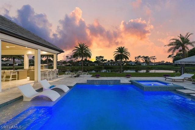 pool at dusk featuring an in ground hot tub, a patio area, and a water view