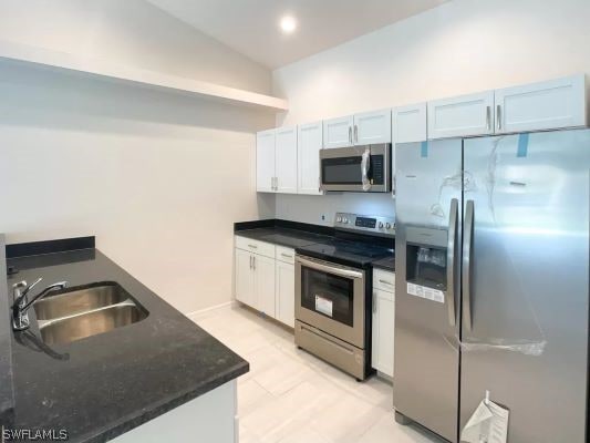 kitchen featuring vaulted ceiling, sink, stainless steel appliances, and white cabinetry