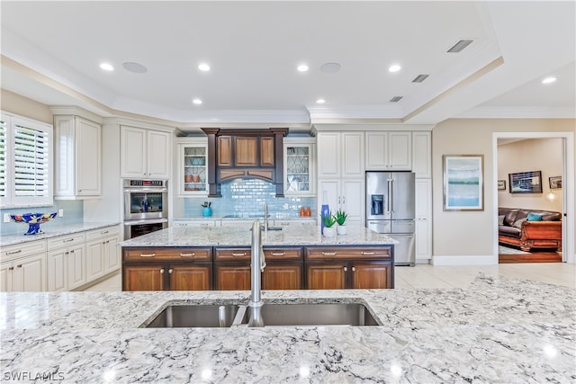 kitchen featuring sink, stainless steel appliances, tasteful backsplash, light stone counters, and an island with sink