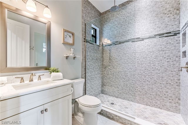 bathroom with a tile shower, tile patterned flooring, vanity, and toilet