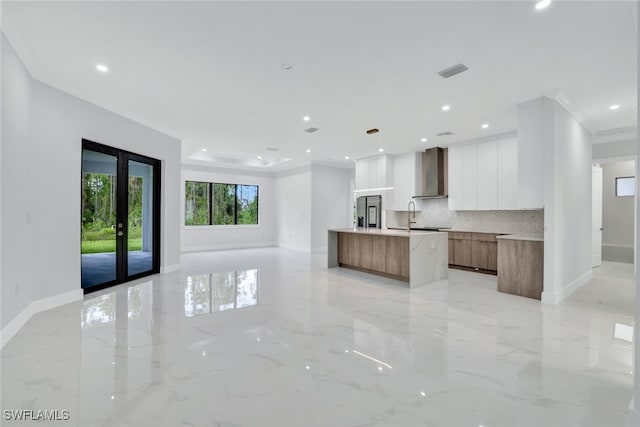 kitchen with tasteful backsplash, white cabinets, ornamental molding, a large island, and wall chimney range hood