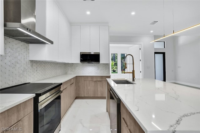 kitchen featuring sink, white cabinetry, wall chimney range hood, stainless steel appliances, and light stone countertops