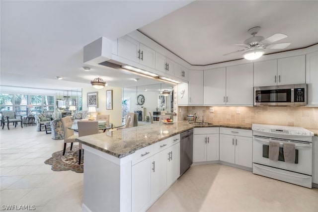 kitchen with tasteful backsplash, white cabinetry, light stone counters, kitchen peninsula, and stainless steel appliances