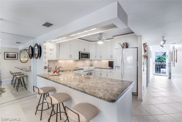 kitchen with white appliances, a breakfast bar, tasteful backsplash, white cabinets, and kitchen peninsula