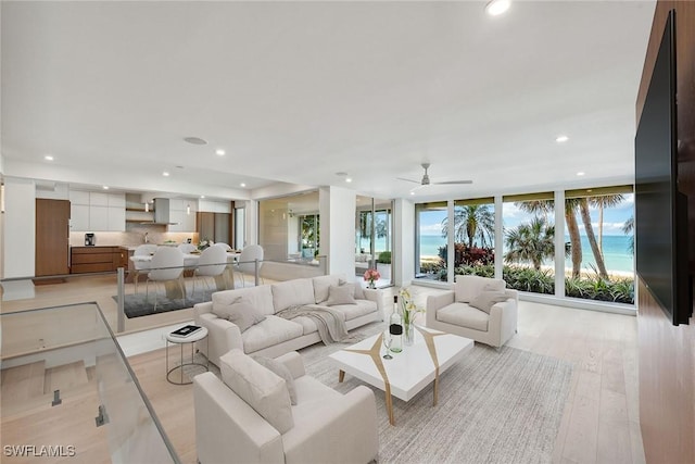 living room featuring ceiling fan, light hardwood / wood-style floors, and a wall of windows