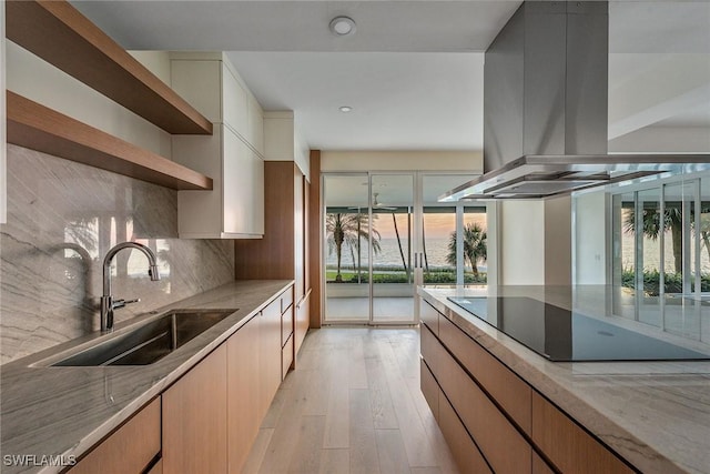 kitchen with sink, light hardwood / wood-style flooring, light stone countertops, black electric cooktop, and island exhaust hood