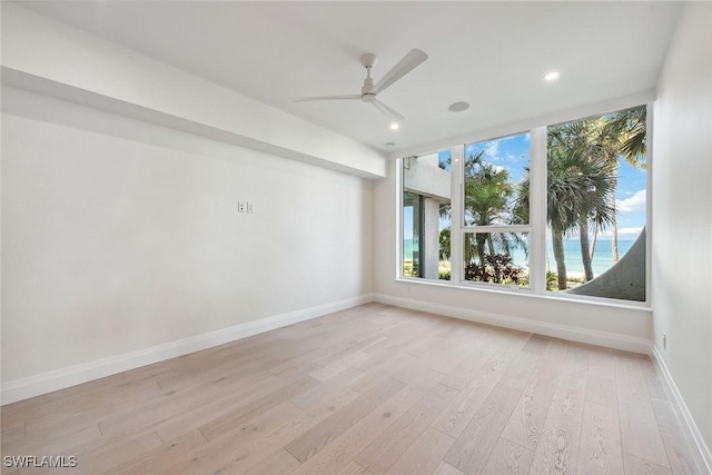 spare room featuring ceiling fan, a water view, and light wood-type flooring