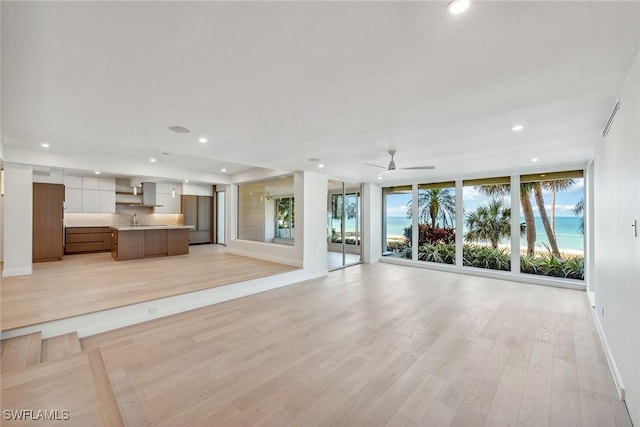 unfurnished living room featuring ceiling fan, sink, expansive windows, and light hardwood / wood-style floors