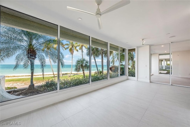 unfurnished sunroom featuring ceiling fan, a water view, and a view of the beach