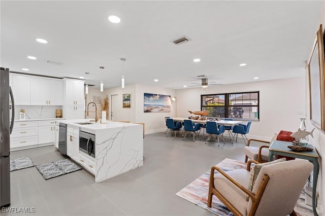 kitchen with white cabinetry, hanging light fixtures, appliances with stainless steel finishes, an island with sink, and light stone countertops