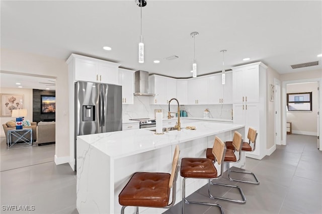 kitchen with white cabinetry, a center island with sink, light stone counters, and wall chimney range hood