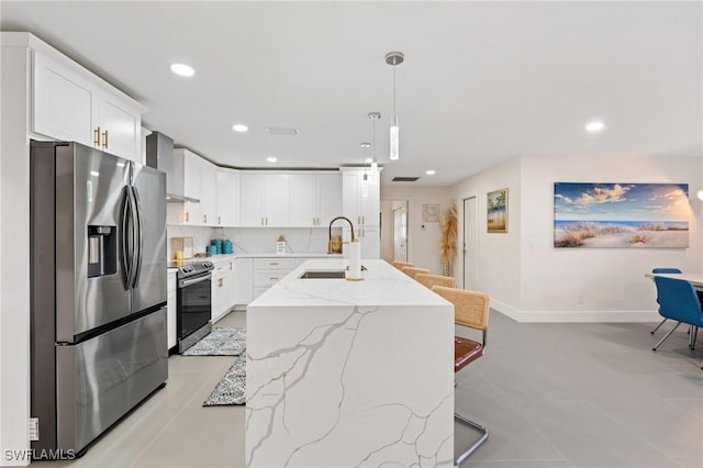 kitchen with white cabinetry, hanging light fixtures, stainless steel appliances, and an island with sink