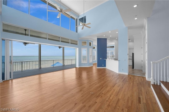 unfurnished living room with hardwood / wood-style floors, a water view, a high ceiling, and sink