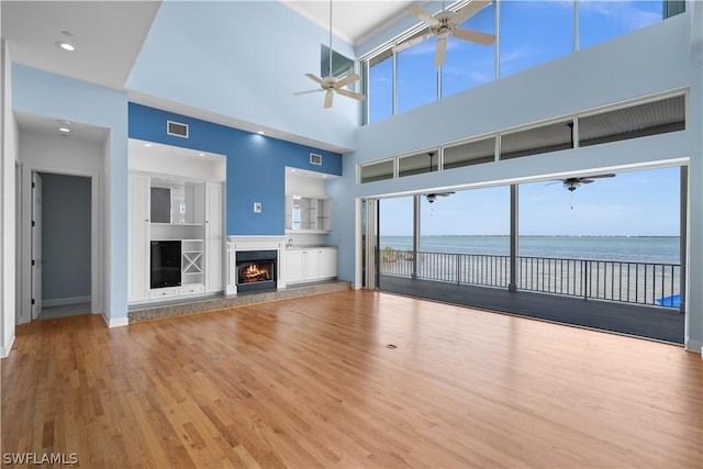 unfurnished living room with hardwood / wood-style floors, a water view, and a high ceiling