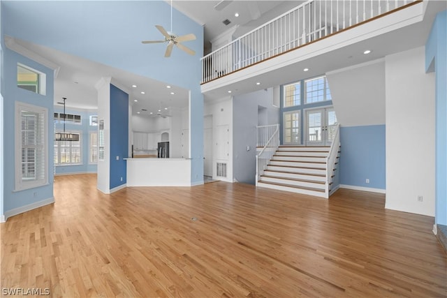 unfurnished living room featuring light wood-type flooring, a towering ceiling, and ceiling fan