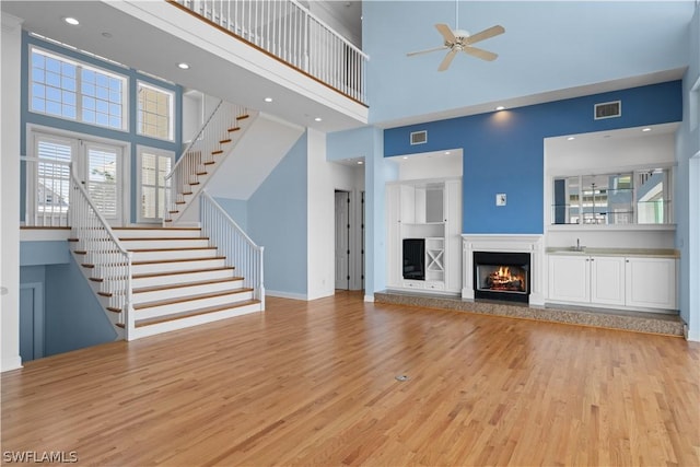 unfurnished living room featuring ceiling fan, a towering ceiling, and light hardwood / wood-style floors