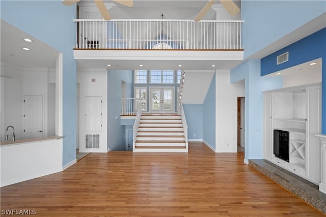 unfurnished living room featuring ceiling fan, a towering ceiling, sink, and light hardwood / wood-style flooring