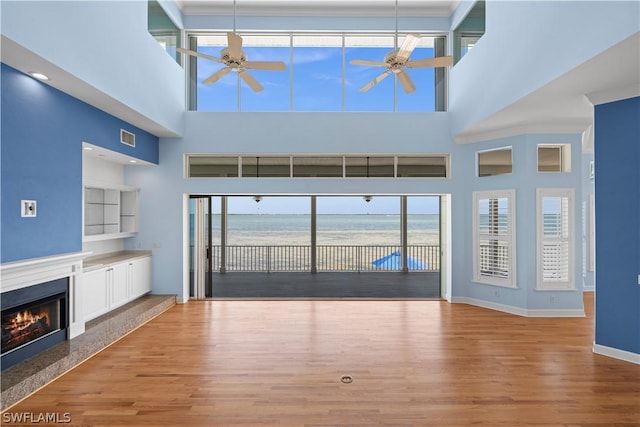 unfurnished living room with a fireplace, a towering ceiling, a water view, and light hardwood / wood-style floors