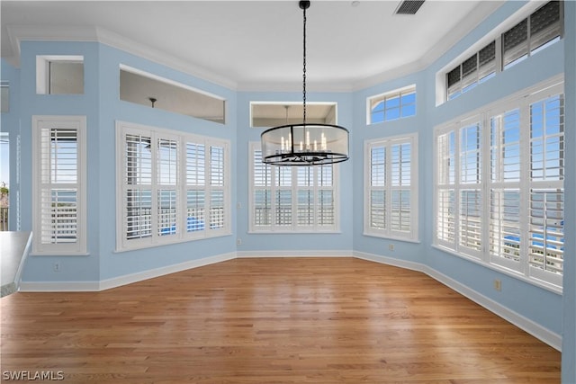 unfurnished dining area with a notable chandelier, a healthy amount of sunlight, wood-type flooring, and crown molding