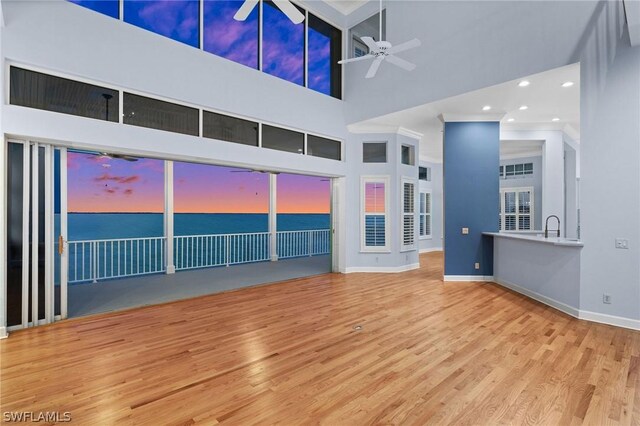 unfurnished living room with ceiling fan, sink, wood-type flooring, and a high ceiling